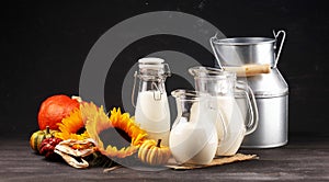 A jug of milk and glass of milk on a wooden table and flower