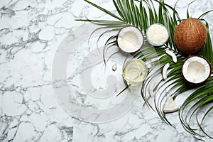 Jug of natural organic oil and coconuts on marble background, flat lay