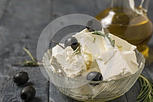 A jug of olive oil and a bowl of feta cheese and olives on a wooden table