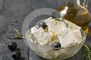 A jug of olive oil and a bowl of feta cheese and olives on a wooden table.