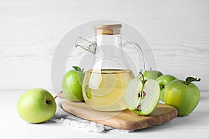 Jug of tasty juice and fresh ripe green apples on white wooden table photo