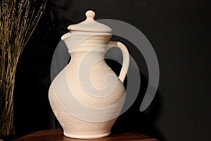 a jug of white clay with a lid on a dark background. old pottery, clay jug