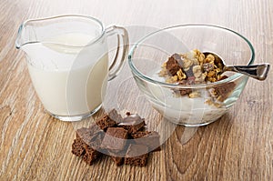 Jug with yogurt, bowl with granola, yogurt, chocolate, pieces of porous chocolate on table