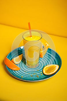 Juice glass and orange fruit on teal plate, orange background