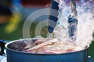 Juicy Angus steak fried in iron cast pan with smoke and Tongs on blurred background