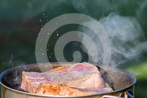 Juicy Angus steak frying in iron cast pan with smoke and Sprinkle salt on blurred nature background