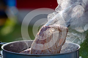 Juicy Angus steak frying in iron cast pan with smoke and Tongs on blurred nature background , cooking party picnic outdoor