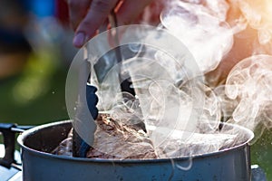 Juicy Angus steak frying in iron cast pan with smoke and Tongs on blurred nature background