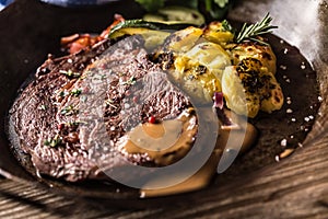 Juicy beef Rib Eye steak roasted potatoes with sauce grilled vegetable salt pepper and herbs in vintage pan