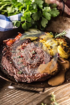 Juicy beef Rib Eye steak roasted potatoes with sauce grilled vegetable salt pepper and herbs in vintage pan