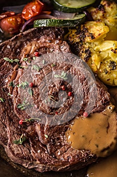 Juicy beef Rib Eye steak roasted potatoes with sauce grilled vegetable salt pepper and herbs in vintage pan