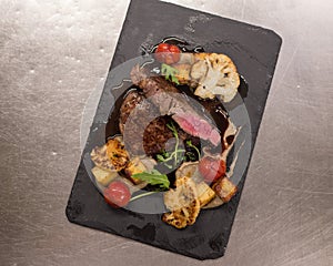 Juicy Beef rump steak from marble beef medium rare with spices and grilled vegetables on black stone plate, close-up