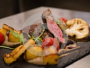 Juicy Beef rump steak from marble beef medium rare with spices and grilled vegetables on black stone plate, close-up