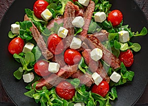 Juicy Beef Sirloin Steak Salad with roasted tomatoes, feta cheese and green vegetables in a black plate. healthy food