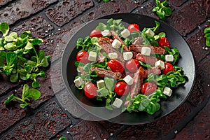 Juicy Beef Sirloin Steak Salad with roasted tomatoes, feta cheese and green vegetables in a black plate. healthy food