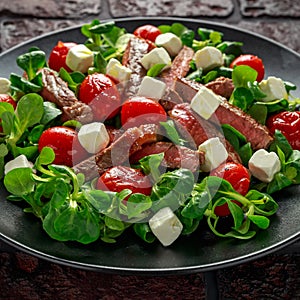 Juicy Beef Sirloin Steak Salad with roasted tomatoes, feta cheese and green vegetables in a black plate. healthy food