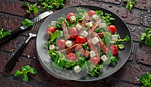 Juicy Beef Sirloin Steak Salad with roasted tomatoes, feta cheese and green vegetables in a black plate. healthy food