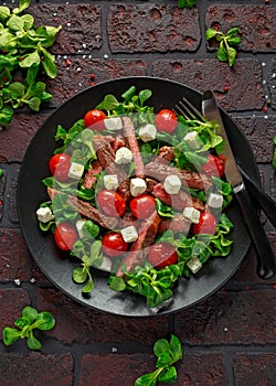 Juicy Beef Sirloin Steak Salad with roasted tomatoes, feta cheese and green vegetables in a black plate. healthy food