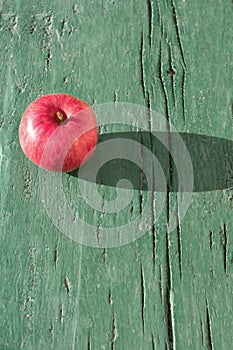 Juicy bright mature red apple on green wooden background on hard light of sunbeams with long dark shadow..Symbol of perfection,