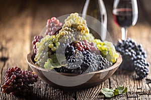 Juicy bunches of grapes in a wooden bowl, red wine in the background