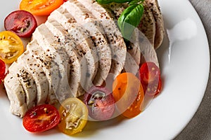 Juicy chicken fillet cooked under vacuum at low temperature. Sliced chicken breast and halves of fresh cherry tomatoes on a white