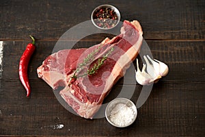 Juicy, fresh, aged t bone steak on a wooden surface with a sprig of rosemary on top, peppercorns, a pod of red chili