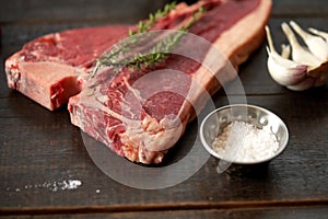 Juicy, fresh, aged t bone steak on a wooden surface with a sprig of rosemary on top, peppercorns, a pod of red chili