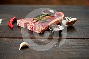 Juicy, fresh, aged t bone steak on a wooden surface with a sprig of rosemary on top, peppercorns, a pod of red chili