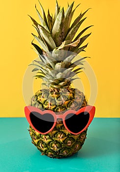 Juicy fresh hipster pineapple with red heart shaped sunglasses on blue and yellow background