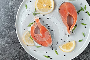 Juicy fresh salmon steak in a white plate with onion lemon and spices on a natural slate stone table