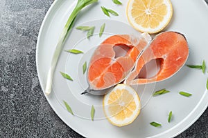 Juicy fresh salmon steak in a white plate with onion lemon and spices on a natural slate stone table close-up