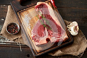 Juicy, fresh, seasoned t bone steak on a wooden cutting board on a piece of burlap with a sprig of rosemary on top, peppercorns