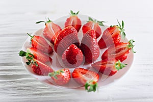 Juicy fresh sliced strawberries on a white plate on a white wooden background