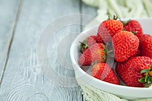Juicy fresh strawberries in a white plate on a grey wooden background, selective focus