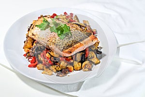Juicy fried rain trout fillet with crispy skin served on vegetables from the oven with parsley garnish on a white plate and napkin