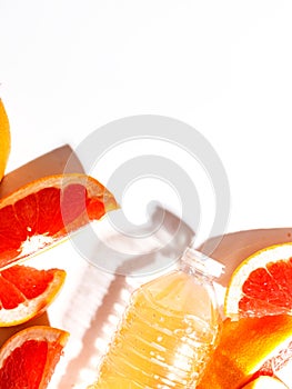 Juicy grapefruit slices and a bottle with juice on a white background. Top view