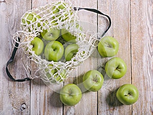 Juicy green apples and cotton string mesh bag on a wooden table. Top view