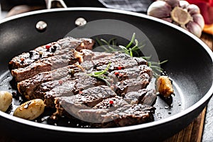 Juicy and grilled beef Rib Eye steak in teflon pan with salt, pepper and rosemary herbs