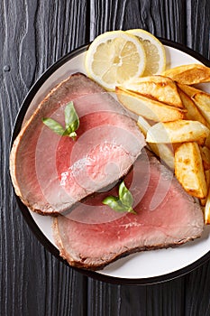 Juicy grilled beef steak with roasted potatoes and lemon close-up on a plate. vertical top view