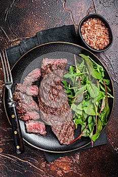 Juicy Grilled Machete skirt beef meat steak on plate with salad. Dark background. Top view