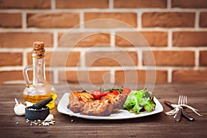 Juicy grilled pork fillet served with cherry tomatoes branch and lettuce on white plate. Background: brick wall. Close-up. Horizon