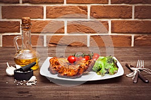 Juicy grilled pork fillet served with cherry tomatoes branch and lettuce on white plate. Background: brick wall. Close-up. Horizon