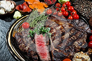 A juicy grilled T-bone steak with vegetables on a black plate