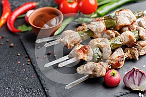 Juicy kebabs from pork on skewers. Meat cooked on open fire and fresh vegetables on a black background. Still life.