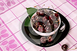 Juicy large dark cherry in a black plate, which stands on a wooden table