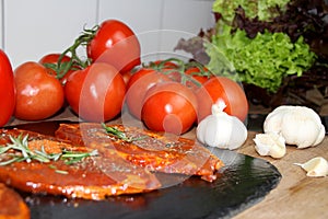 Juicy marinated with spices raw meat on a black board in the kitchen, steaks with rosemary, red tomatoes, paprika, garlic, concept