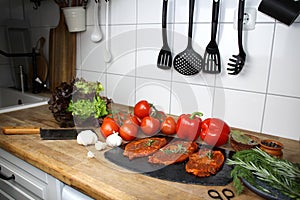 Juicy marinated with spices raw meat on a black board in the kitchen, steaks with rosemary, red tomatoes, paprika, garlic, salad,