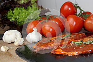 Juicy marinated with spices raw meat on a black board in the kitchen, steaks with rosemary, red tomatoes, paprika, salad, concept