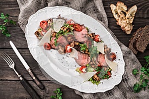 Juicy medium beef fillet steaks mignon with grilled vegetables, mushrooms, tomatoes, cheese in plate on rustic wooden background