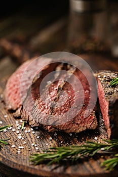 Juicy medium Beef Rib Eye steak slices on wooden board with herbs spices and salt